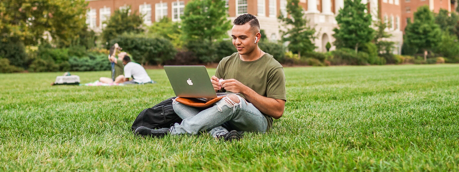 A student sits outside working on his computer