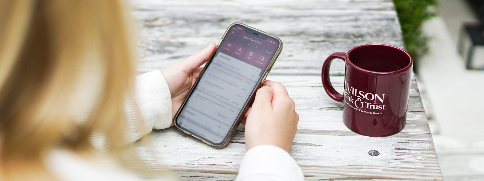 A woman looking at her Bank  app with a mug next to her.